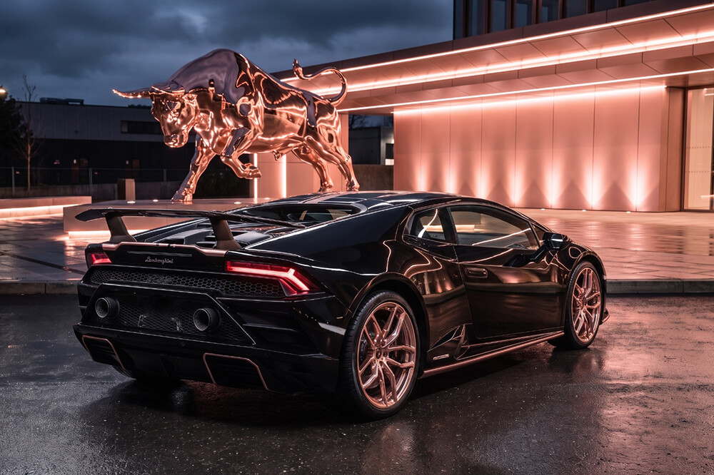 Black Lamborghini sports car parked at night in front of a glowing bull statue.